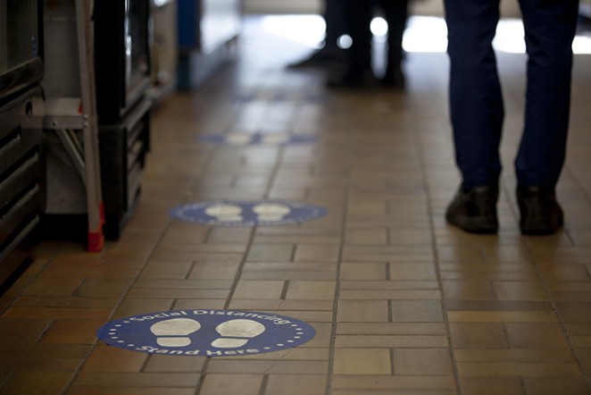 People stand besides floor stickers that encourage social distancing. - GOTOVAN ON FLICKR