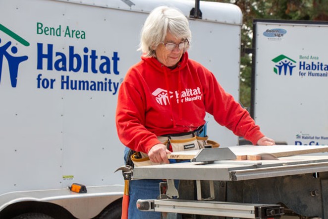 Ann Kelly, a volunteer with Bend Area Habitat for Humanity, uses a table saw to modify a cabinet shelf at the new construction site Monday. The nonprofit is building two new homes at NW 17th Street and NW Hartford  Street. - KEELY DAMARA