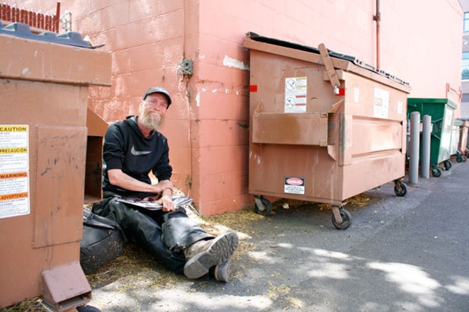 Bill Smith sits between two dumpsters in the alleyway by Pedego Electric Bikes in Bend. - CHRIS MILLER