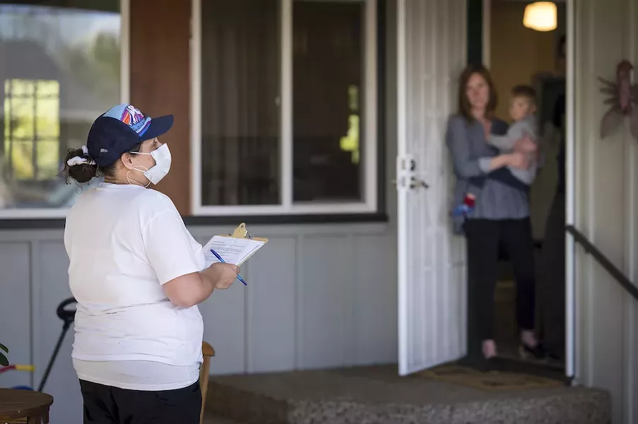 A field staff member for OSU's TRACE-COVID-19 project stands at a distance from the woman she is about to ask to volunteer to take the test. Participants leave completed tests outside. - OREGON STATE UNIVERSITY