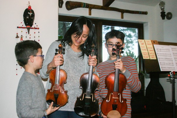 It's all in the family: Brothers Ezra and Nicolas Oncken, of Sisters, discuss the many sizes of violins with their mom, Akiko, in their home, just before evening practice. - JIM ANDERSON