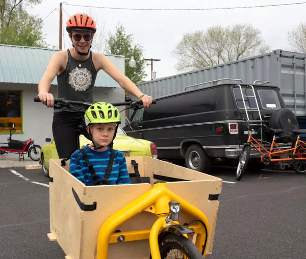 Willow Hamilton rides Aidan Miller around in a Bakfiets-style bike in the parking lot of Bend Electric Bikes. - CHRIS MILLER