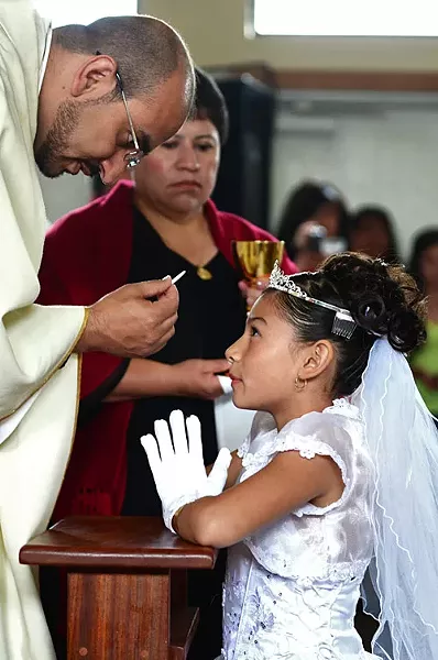 "A young girl receives a spiritual meal, her first communion in the Catholic church" by Trevor Normile