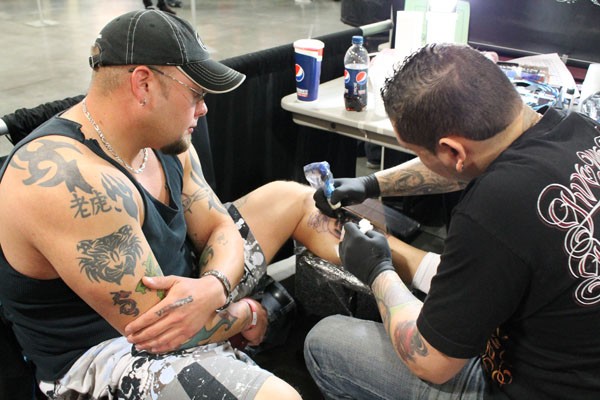 Calvin Youngblood watches on as Flaco Garcia, Hard Know Tattoos from Bronx, NY, creates tattoos his calf.