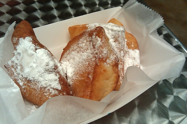 Fresh beignets are covered in powdered sugar.