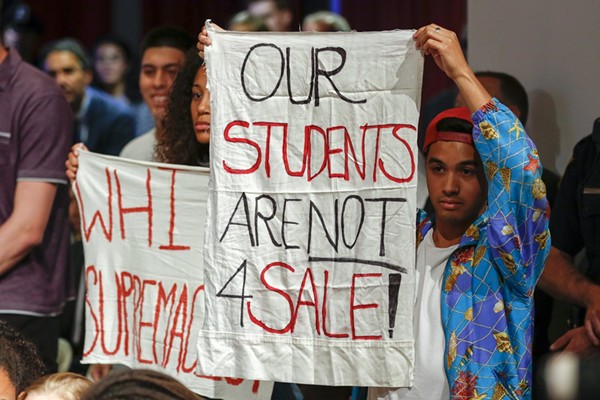Quisol (right) holds up a sign protesting a speech by Trump's Education Secretary Betsy DeVos at Harvard in September 2017.