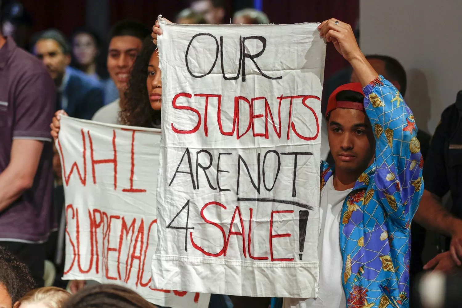 Quisol (right) holds up a sign protesting a speech by Trump's Education Secretary Betsy DeVos at Harvard in September 2017.