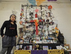 Teresa Hernandez, owner of Pura Vida Worldy Art, in front of a shrine she has kept in her store since holding a Dia de los Muertos celebration nearly a decade ago. (Photo by Ryan Pitkin)