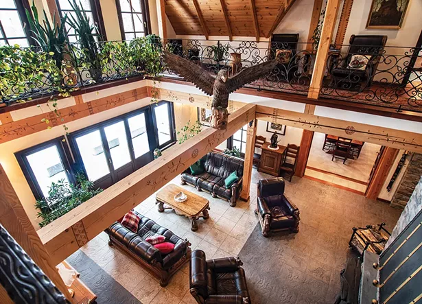 The two-story main living room of the Laroux family’s traditional Zakopane chalet was inspired by the distinctive architecture of Podhale—the Southern Polish Highland region of Eastern Europe’s Carpathian Mountains. The ornate wood-carved beams, the metal railings, and the Polish White Eagle statue are quintessential features of the Zakopanski vernacular, and the space is decorated with furniture imported from Poland. Interspersed with more traditional oil paintings of the Polish countryside are Jack Laroux’s own large acrylic on canvas abstract works. - PHOTO BY DEBORAH DEGRAFFENREID