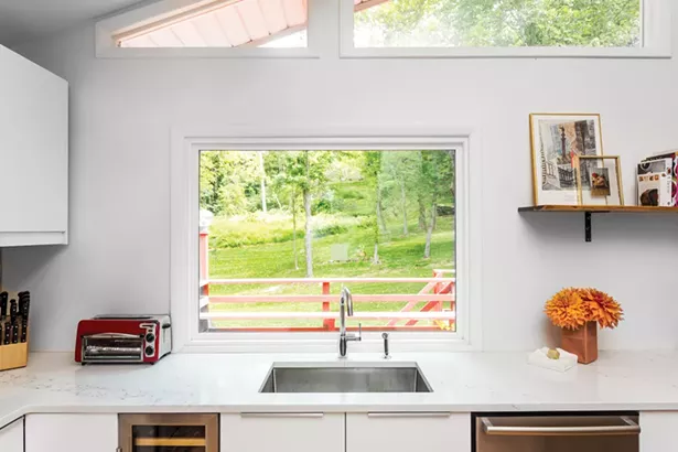 The renovated kitchen looks out through windows and sliders to the lawn and woods behind the house. The couple is divided over which room in the house is the best place to sit. “Each area offers a different experience,” says Schultz. “ Aaron loves the dining room in back because it’s nested and you can hear birds in the nearby trees, but still see the views further away. I love the front because it’s closer to the river.” - PHOTO BY WINONA BARTON-BALLENTINE