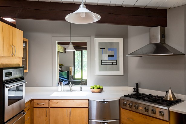 The home’s kitchen was remodeled by the home’s previous owners, avid cooks, with stainless steel appliances, wood cabinets, and clean white countertops. The open-concept space looks into a bonus room, outfitted as an office and TV lounge for Hemphill. The modernist, geometric print on the wall was painted in 2016 by Nathalie Du Pasquier. - WINONA BARTON-BALLENTINE