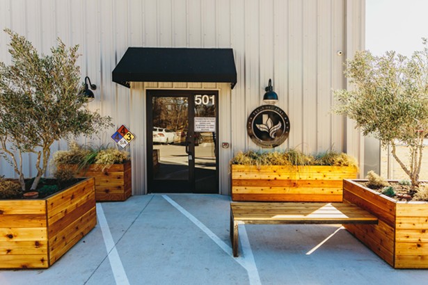 The exterior of Texas Original Cannabis Company (TOCC). An activated retail entry adds ambiance to the nondescript metal agricultural structure.