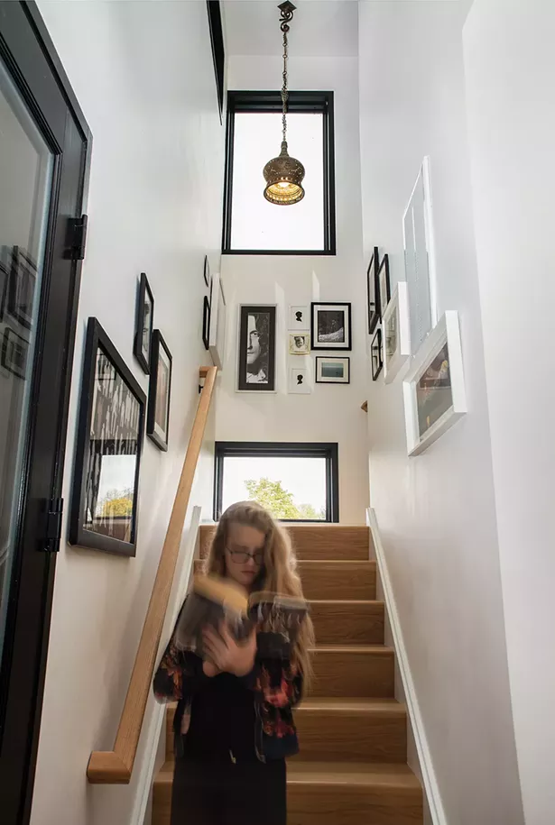 Schmidt’s daughter descending the stairs. Her 12’-by-12’ foot room upstairs has a distinctive feature: She can climb out the window under the home’s overhang to enjoy her own private outdoor reading nook. The stairs are decorated with local artwork, including paper-cut silhouettes by Jenny Lee Fowler of Port Ewen and a pencil drawn portrait of Robert Plant by Raphiel O’Connor of Rhinebeck. - PHOTO: DEBORAH DEGRAFFENREID