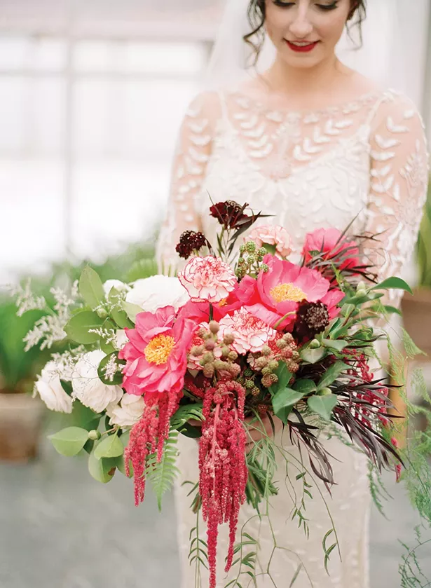 A wild, winter bridal bouquet with peonies, unripe raspberries, ranunculus, scabiosa, hanging amaranthus, camellia, limonium, antique carnations, ferns and cascading pepper berry foliage. - COURTESY OF DARK + DIAMOND