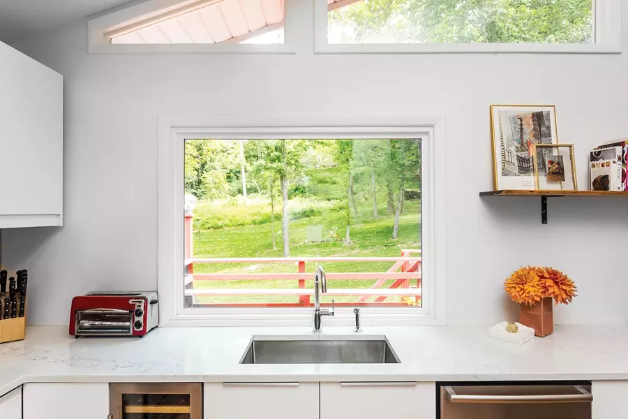 The renovated kitchen looks out through windows and sliders to the lawn and woods behind the house. The couple is divided over which room in the house is the best place to sit. “Each area offers a different experience,” says Schultz. “ Aaron loves the dining room in back because it’s nested and you can hear birds in the nearby trees, but still see the views further away. I love the front because it’s closer to the river.” - PHOTO BY WINONA BARTON-BALLENTINE
