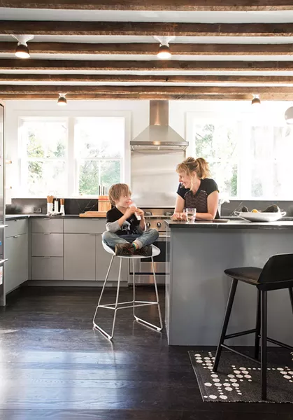 Dunja Von Stoddard and her son Lars in the kitchen. The space was rebuilt from the ground up (including the south facing back wall, which had sustained fire damage and needed to be completely replaced), but the wooden ceiling beams are original. “I wanted to bring it back in a modern way that was still appreciative of an old farmhouse,” says Von Stoddard. - DEBORAH DEGRAFFENREID