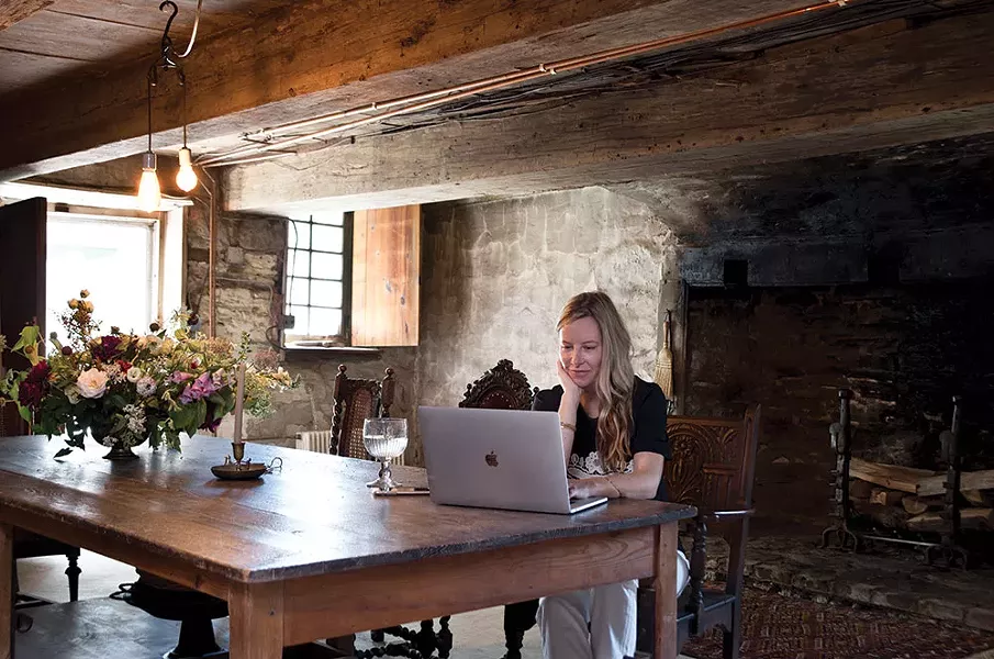 Designer Caroline Diani in the dining room of her 18th-century stone house. Refurbishing the historic property has stoked her creative fire. Here she’s surrounded a French draper’s table with antique chairs, all from the 19th century; the fireplace features 17th-century French andirons. - DEBORAH DEGRAFFENREID