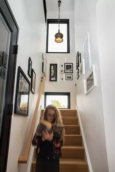 Schmidt’s daughter descending the stairs. Her 12’-by-12’ foot room upstairs has a distinctive feature: She can climb out the window under the home’s overhang to enjoy her own private outdoor reading nook. The stairs are decorated with local artwork, including paper-cut silhouettes by Jenny Lee Fowler of Port Ewen and a pencil drawn portrait of Robert Plant by Raphiel O’Connor of Rhinebeck. - PHOTO: DEBORAH DEGRAFFENREID