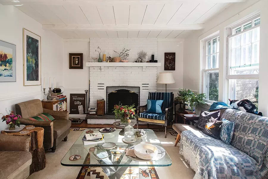The living room of Hammer and Lafferty’s home includes a working fireplace, views to the abundant perennial garden, and an assortment - of furniture and art. “Melina has a penchant - for one-of-a-kind, eclectic pieces largely incorporating weathered and worn elements: well used old cutting boards, retooled chairs, antique transferware and ironstone china, and vintage rugs from places around the world,” says Lafferty. - PHOTO: DEBORAH DEGRAFFENREID