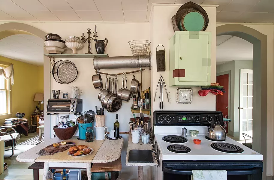 In the kitchen, Feinberg removed a wood - burning cook stove but kept the stove pipe, reappropriating it as a hanging pot rack. Inspired by paint swatches, she repainted the cabinets with random, geometric splashes of color. The experiment in kitchen redecorating then worked its way into her creative work, with similar geometric squares of varied color showing - up in her oil paintings. “It really diverged from the type of work I had been doing years before,” she explains. - PHOTO: DEBORAH DEGRAFFENREID