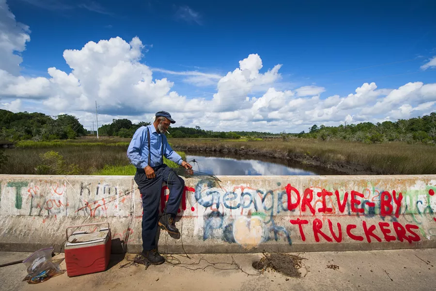 "This was shot on a bridge on the historic Liberty Trail in Liberty County. That's actually the old Liberty Canal. Parts of the Liberty Trail are current roadway, but parts of it, like this, are pretty much off the grid and basically deserted. The man was the only person in eyesight. He initially didn't want me to take his picture. But I hung out with him for a few minutes, sort of chatted awhile. Then I asked again and he said okay. If you look closely you can see he's smiling in the photo—he knows the camera is on him. I really like this because you've got colorful touches like the blue of the sky, the words Georgia Peach with an actual peach painted over it later, and the Drive By Truckers."