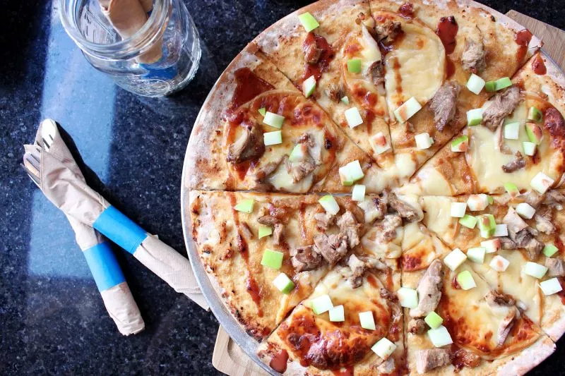 Duck Confit Pizza Pie, topped with melted smoked gouda, slow cooked duck, onion marmalade, diced green apple served with drizzled blueberry vinaigrette.