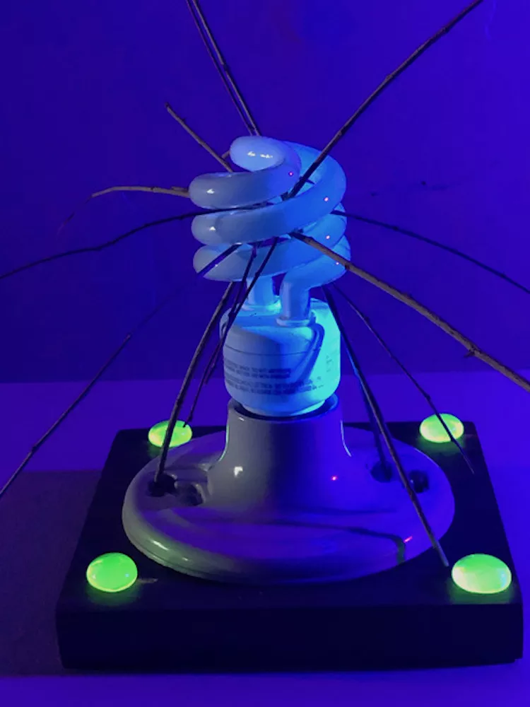 Steven Shugart, “A Little Poem,” fluorescent light bulb, twigs, lamp holder, padauk, uranium glass beads, brass screws under black light. - STEVEN SHUGART