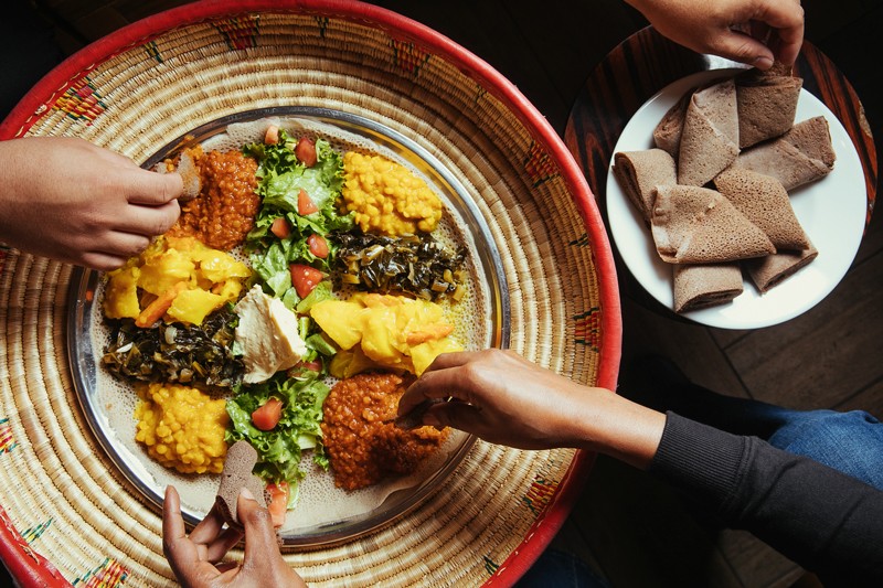 A classic veggie combo — misir wot, gomen, kik alicha, atakilt, and a salad topped with buticha — being shared at Cafe Romanat. - ANDRIA LO