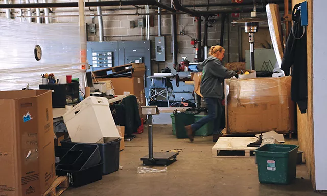 Tracy Bixler rummages through a box in BLH’s special project section. Companies such as Bunn and Mercedes Benz send equipment to BLH in order to be broken down and destroyed to prevent their parts being sold on Ebay and the Grey Market for resale. - PHOTO BY BRANDON TURLEY