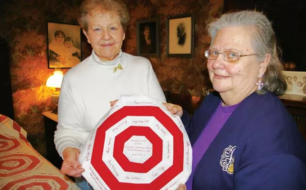 Vachel Lindsay Home State Historic Site administrator Jennie Battles, left, and Prairie Arts Chapter Embroiderer’s Guild of America president Hope Wright hold a piece of the new quilt that the VLH is replicating from a 1912 quilt, shown to th - PHOTO BY ANITA STIENSTRA
