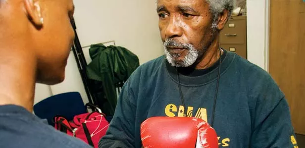 Boxing coach Luther Howell laces up the gloves of a young man in the SHA Cobras boxing club. - PHOTO BY PATRICK YEAGLE
