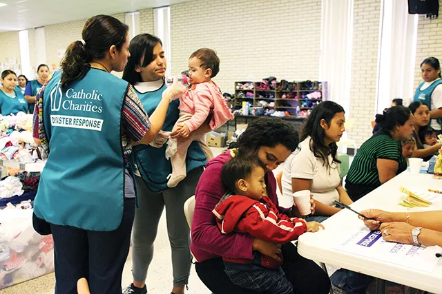 Two volunteers with a Catholic Charities disaster relief team give a Central American refugee baby a bottle containing pedialyte, while a mother offers her young son a cup of water at the reception hall of Sacred Heart Catholic Church where they will rece