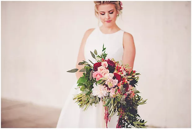 Bride Kaitlin Dietrich had a clutch bouquet with a waterfall in front. The flowers include peonies, hyperricum berries, roses, cushion mums, seeded eucalyptus, Italian ruscus and olive foliage. - PHOTO BY KARA EVANS PHOTOGRAPHY