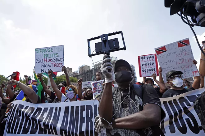 A man uses a bracket to hold his cell phone camera as he records speakers during a Caribbean-led Black Lives Matter rally at Brooklyn's Grand Army Plaza, Sunday, June 14, 2020, in New York. - AP PHOTO/KATHY WILLENS