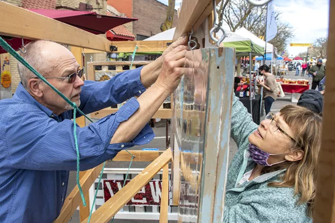 Pullman artist Pamela Arborgreen gets some help hanging some of her artwork in her booth at Moscow’s first farmers market last year. - ZACH WILKINSON/INLAND 360