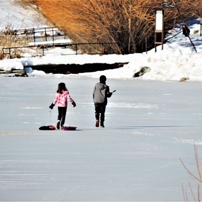 A couple of children playing on the thick icy surface of the Spring Valley Reservoir near Troy, Idaho on Sunday, January 23, 2022.  The boy on the right is holding the head of a cattail plant which he and his sister later released the fuzzy parts of the cattail into the air and watch them sail away in the wind.