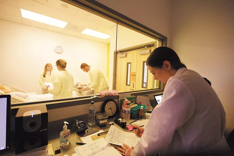 Behind a one-way mirror, Clinical Assistant Professor Kim McKeirnan takes notes as students (left to right) Julie McCullough, Aubrie Widhalm and Kyle Roberts practice their physical assessment skills. - YOUNG KWAK