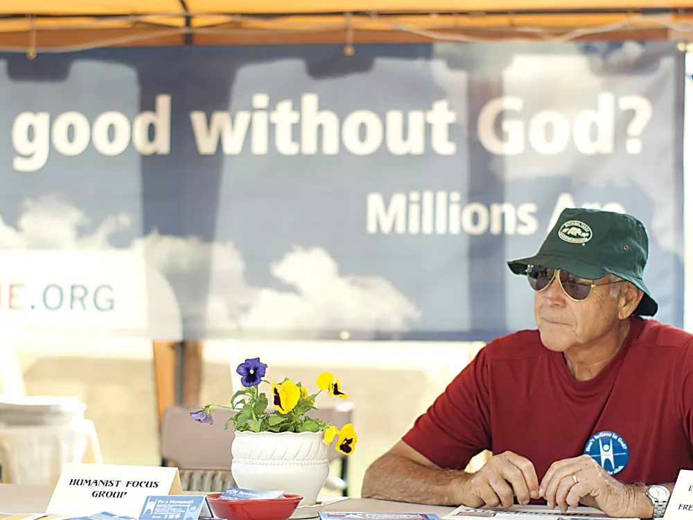 Dick Gammon, member of the Inland Northwest Humanists, reads the Freethought Today newspaper while tending the booth. - MIKE MCCALL