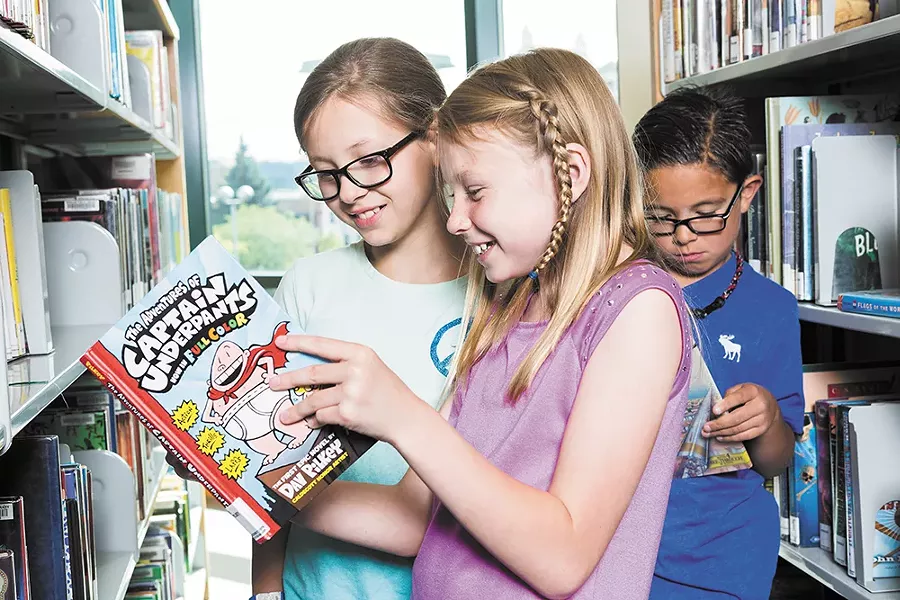Faith and Addie share a Captain Underpants book at the downtown Spokane Library. - STEPHEN SCHLANGE