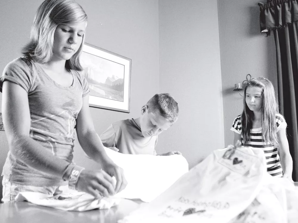 From left, Sarah, Thomas and Emily Kladar tie towels to sell for their charity. So far, they've sold more than 6,000 of them. - YOUNG KWAK
