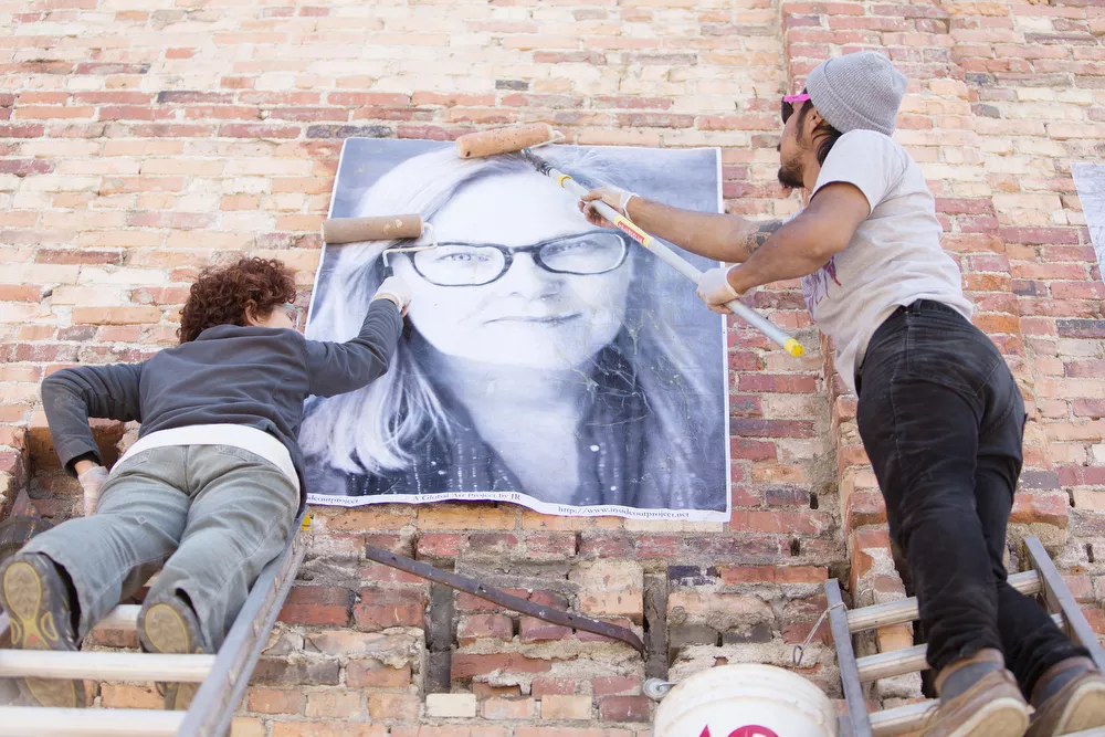 Organizer Susan Jane Hall, left, and volunteer Jose Villa paste a photograph of Laura onto a wall. - YOUNG KWAK