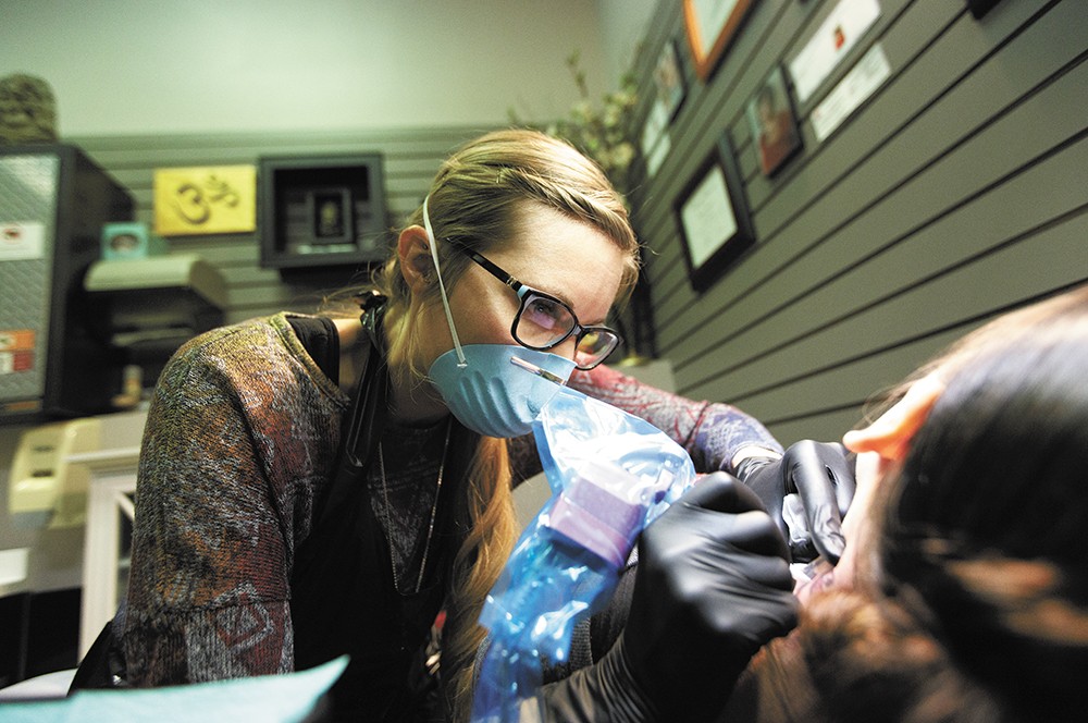 Owner Jacque Gibson Kloehn works to remove a tattoo from Evelyn’s neck at Silver Safari in the Spokane Valley Mall. - YOUNG KWAK