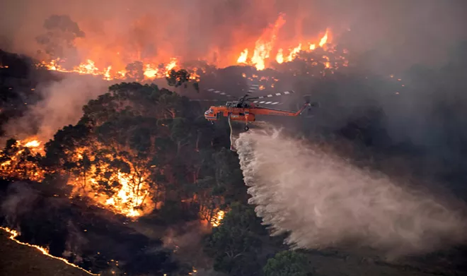 A photo provided by the State Government of Victoria, Australia, shows a helicopter dumping water on a wildfire near Bairnsdale on Tuesday, Dec. 31, 2019. The country’s east coast is dotted with apocalyptic scenes on the last day of the warmest decade on record in Australia. - STATE GOVERNMENT OF VICTORIA VIA THE NEW YORK TIMES