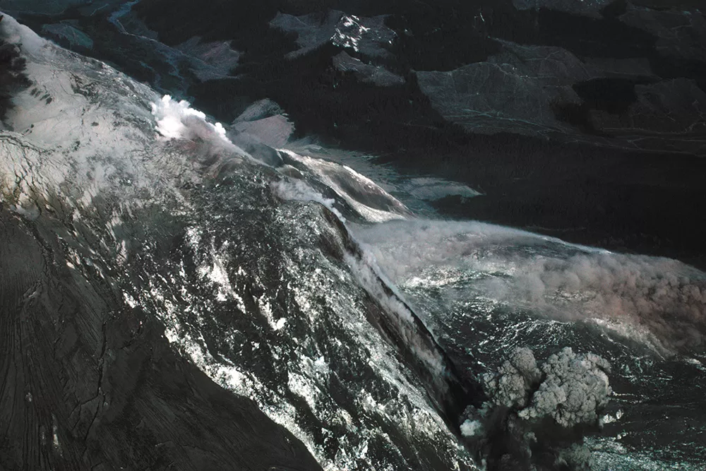 An aerial view as the massive, earthquake-triggered landslide began. The north side of the mountain crumbled away, causing the initial eruptive blast to occur simultaneously out of the volcano's flank and crater. - KEITH AND DOROTHY STOFFEL PHOTO