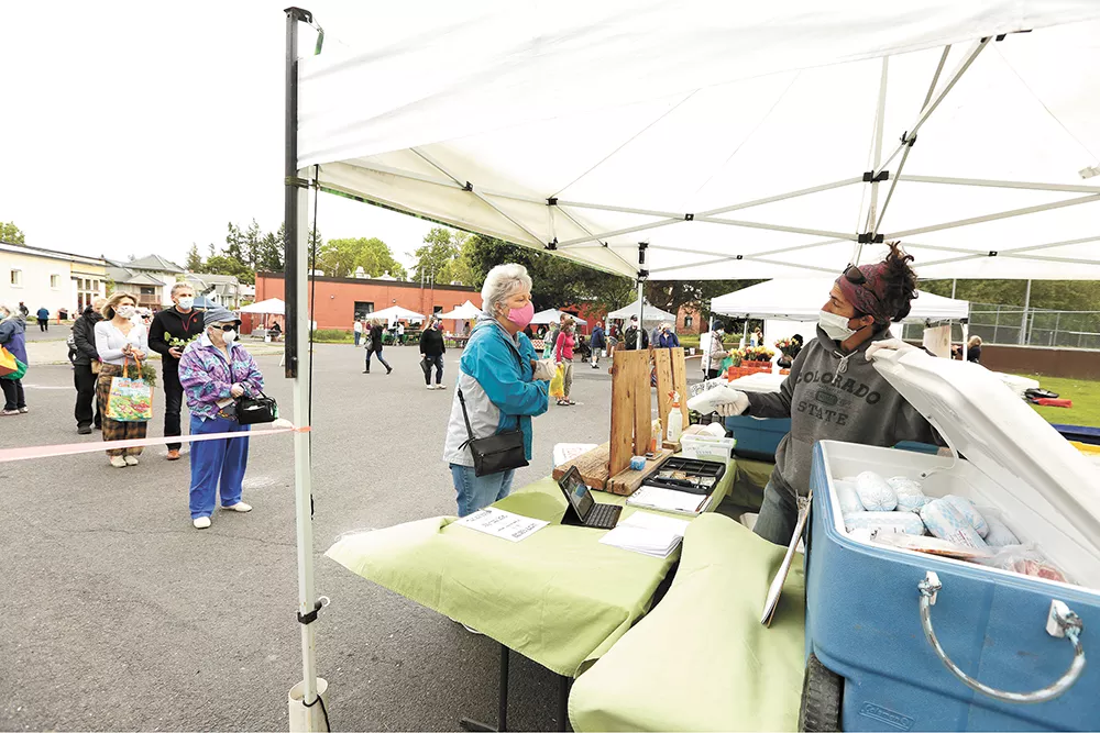 Ramstead Ranch co-owner Eileen Napier (right) shows a pork steak to Deb Brady as other customers wait on markers meant to encourage social distancing at the South Perry Thursday Market. - YOUNG KWAK PHOTO