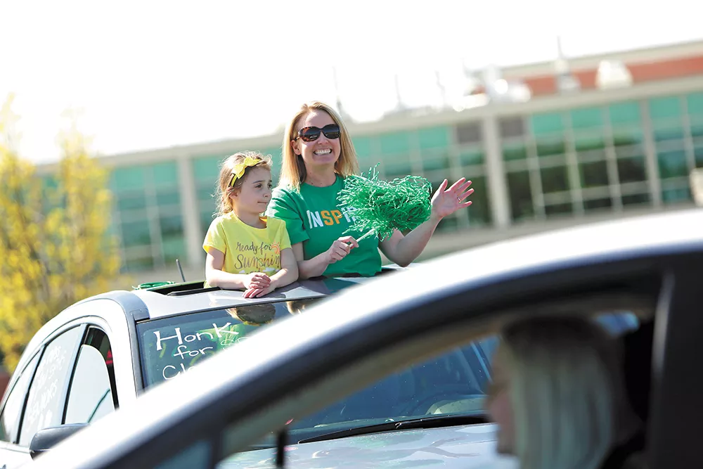 Shadle Park High School counselor Stephanie Filippini, right, and her 6-year-old daughter, Chloe, greet seniors as they arrive to pick up their caps and gowns on May 8 during a drive-up event. - YOUNG KWAK PHOTO