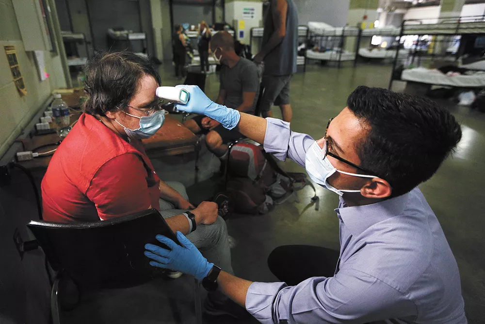 Mohammad Keshtkar checks Amanda Stockton's temperature while conducting a COVID-19 screening at the Spokane Veterans Memorial Arena, which is hosting a temporary shelter for homeless people. - YOUNG KWAK PHOTO