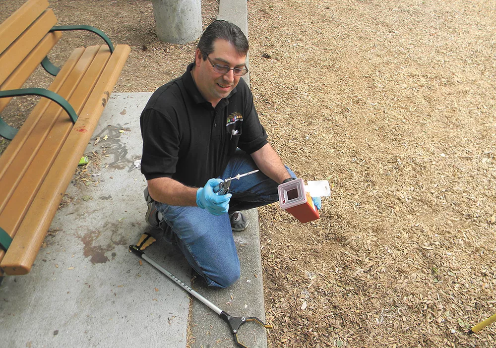 David Byrnes, of the West Central Community Center, uses a Leatherman to pick up a syringe at A.M. Cannon Park. - JAKE THOMAS