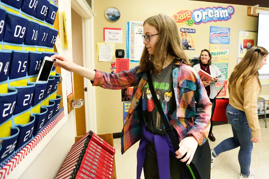 13-year-old Emelia Sanburn picks up her cell phone from a holder after class. - YOUNG KWAK