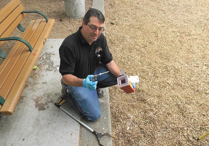 David Byrnes, of the West Central Community Center, uses a Leatherman to pick up a syringe at A.M. Cannon Park. - JAKE THOMAS